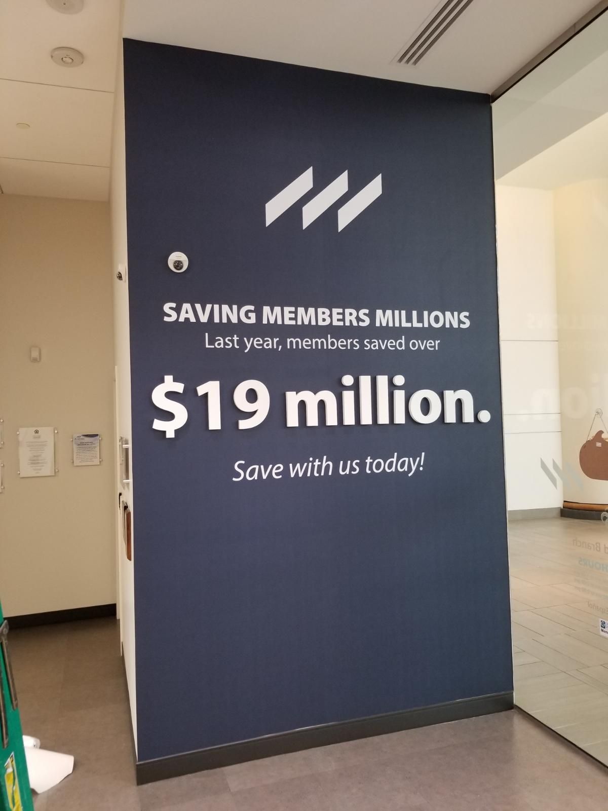 Dark blue wall sign reads “SAVING MEMBERS MILLIONS $19 million. Save with us today!”