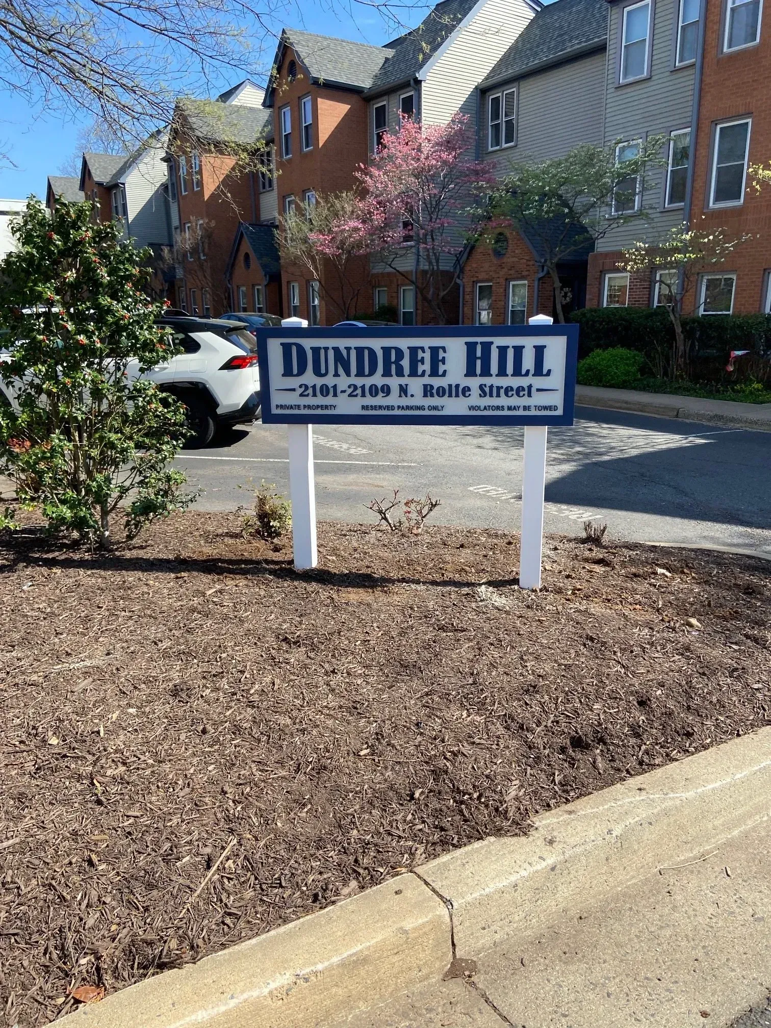 Dundee Hill apartment sign in front of brick buildings and a parked car on a sunny day