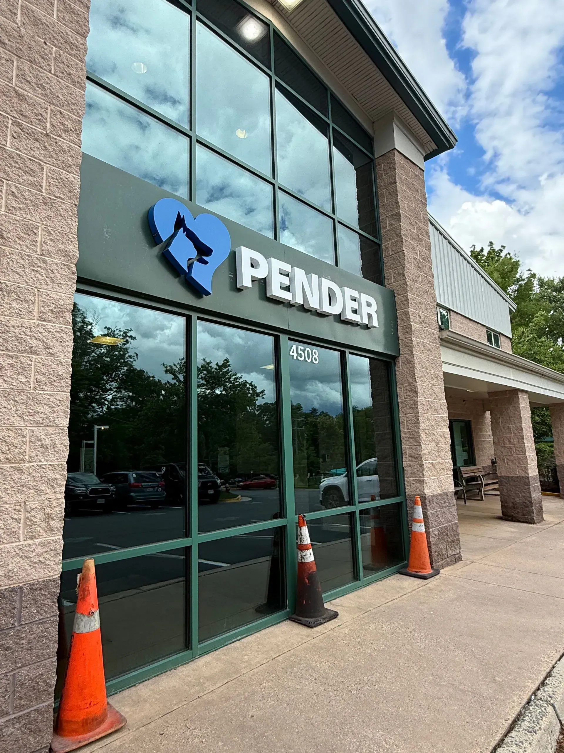 The storefront of Pender Veterinary Centre with a blue heart-shaped logo, glass windows, and orange traffic cones.