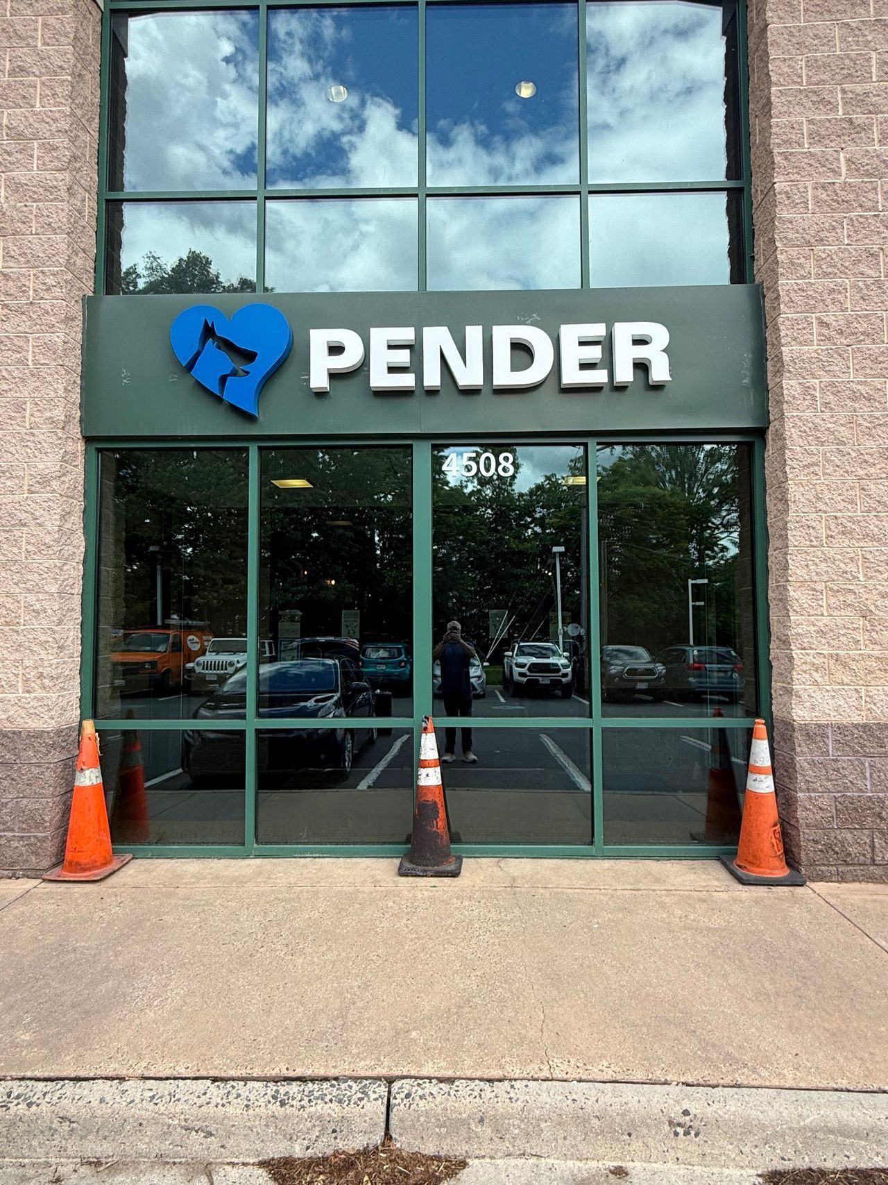 Pender storefront with glass doors, blue logo, and orange traffic cones outside