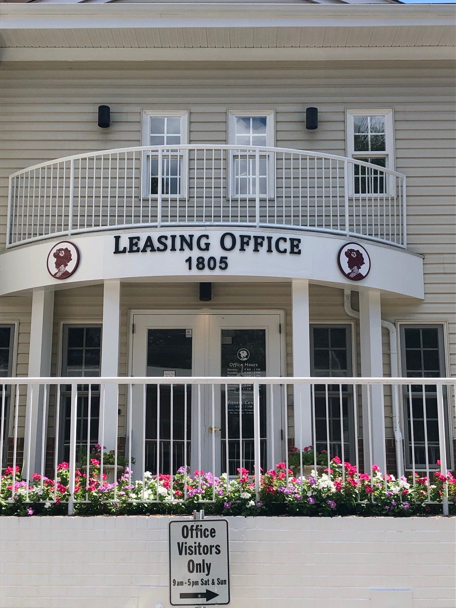 Leasing office entrance with white balcony, black lettering, and flower beds in front