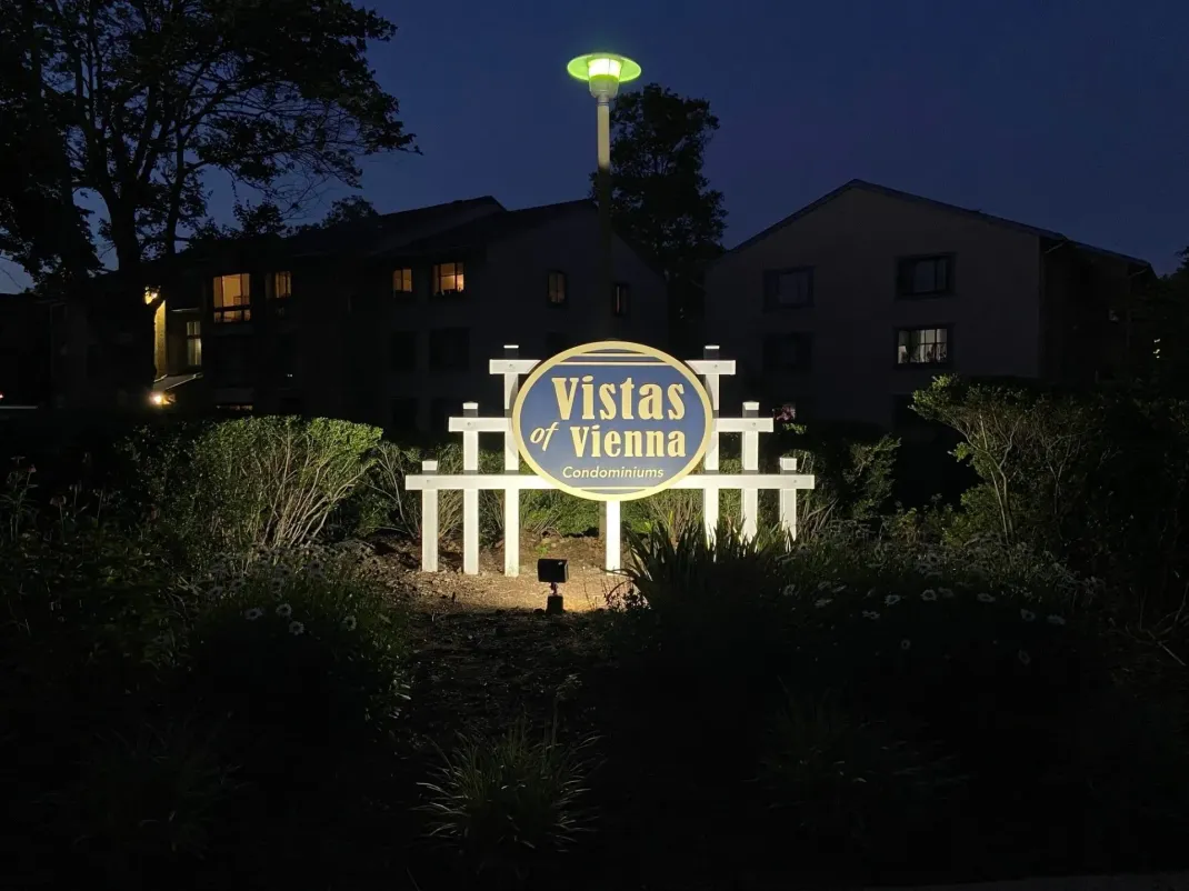 Illuminated sign for "Vistas of Vienna" residential community, surrounded by dark landscaping at night.