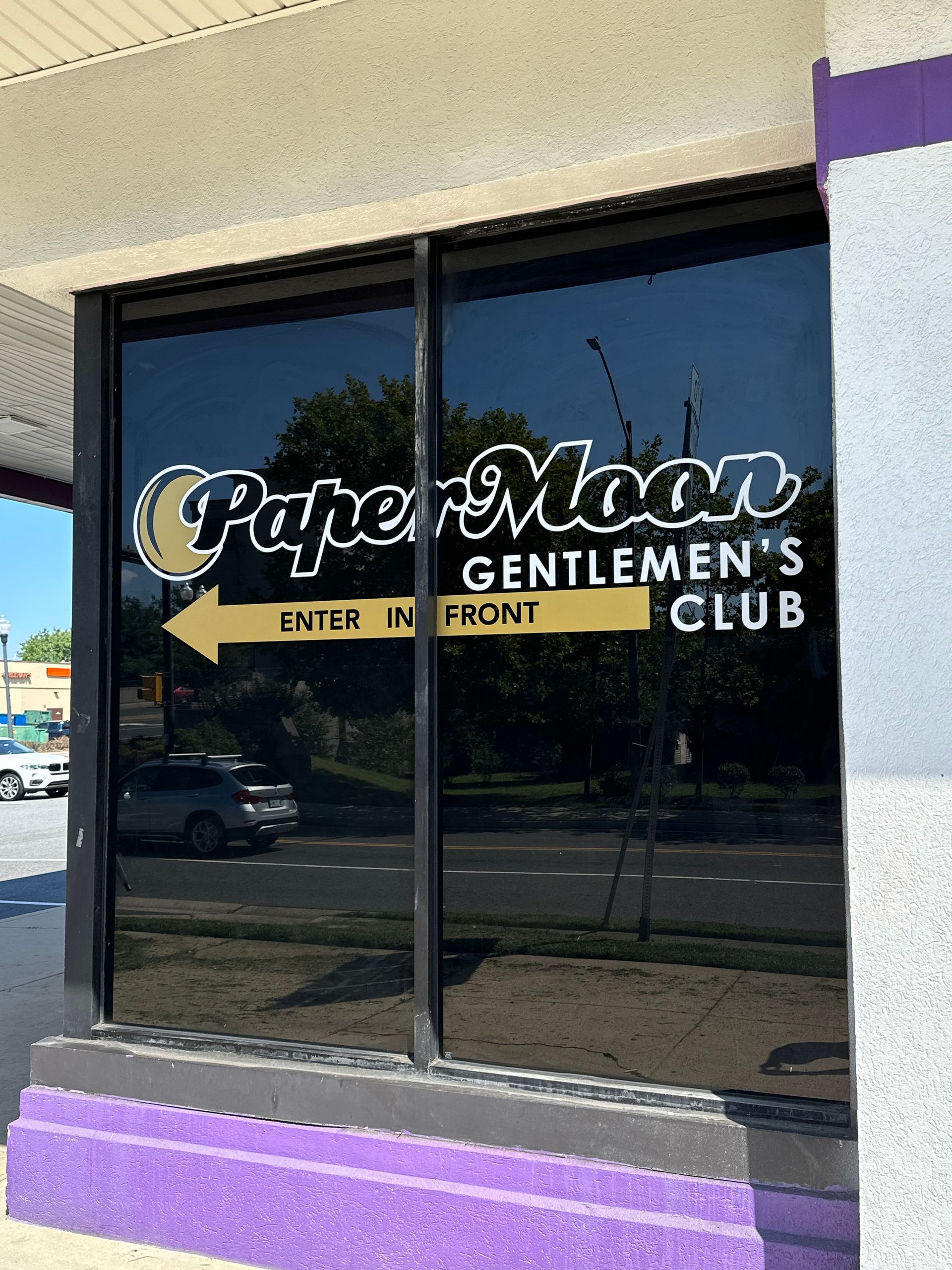 Paper Moon Gentlemen’s Club sign on a storefront window with a yellow “Enter in front” arrow and purple trim