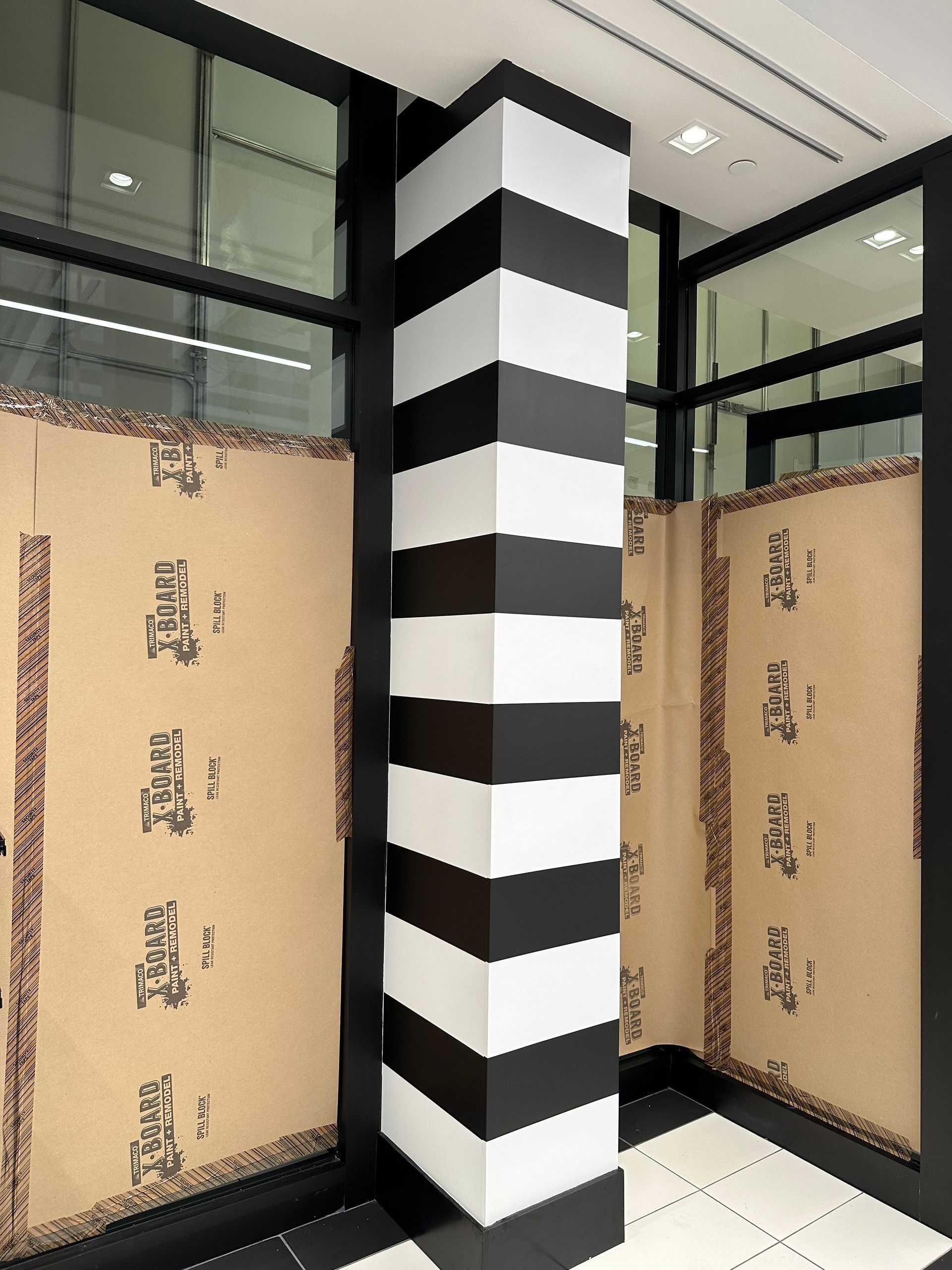 A black and white striped pillar stands between two glass panels covered with brown paper inside a modern store.