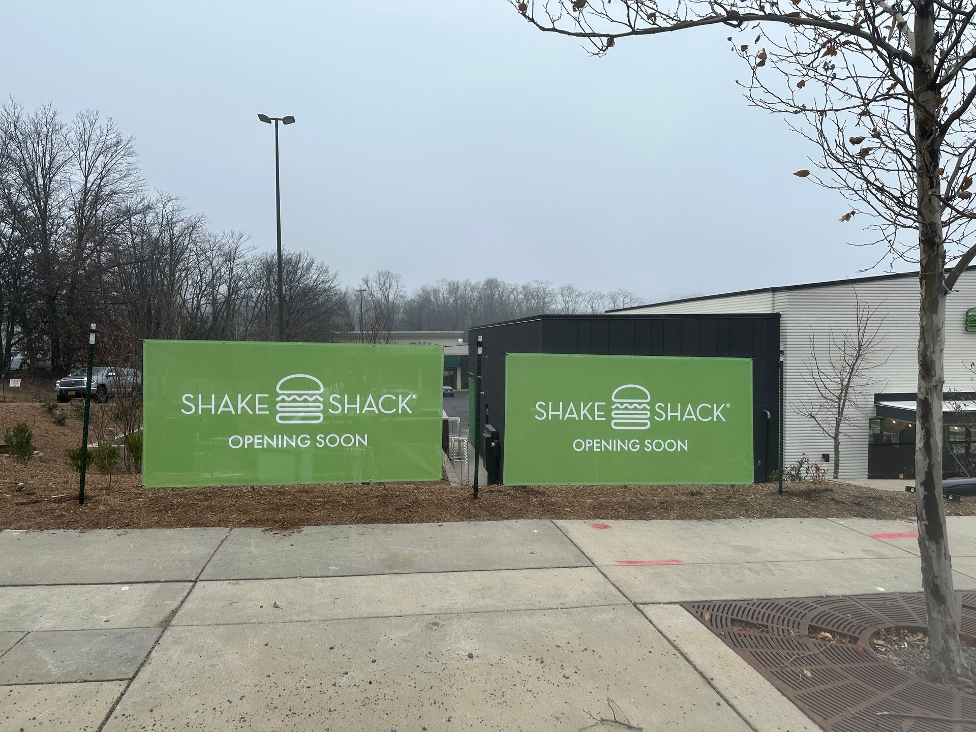 Green Shake Shack construction signs beside a sidewalk on an overcast day