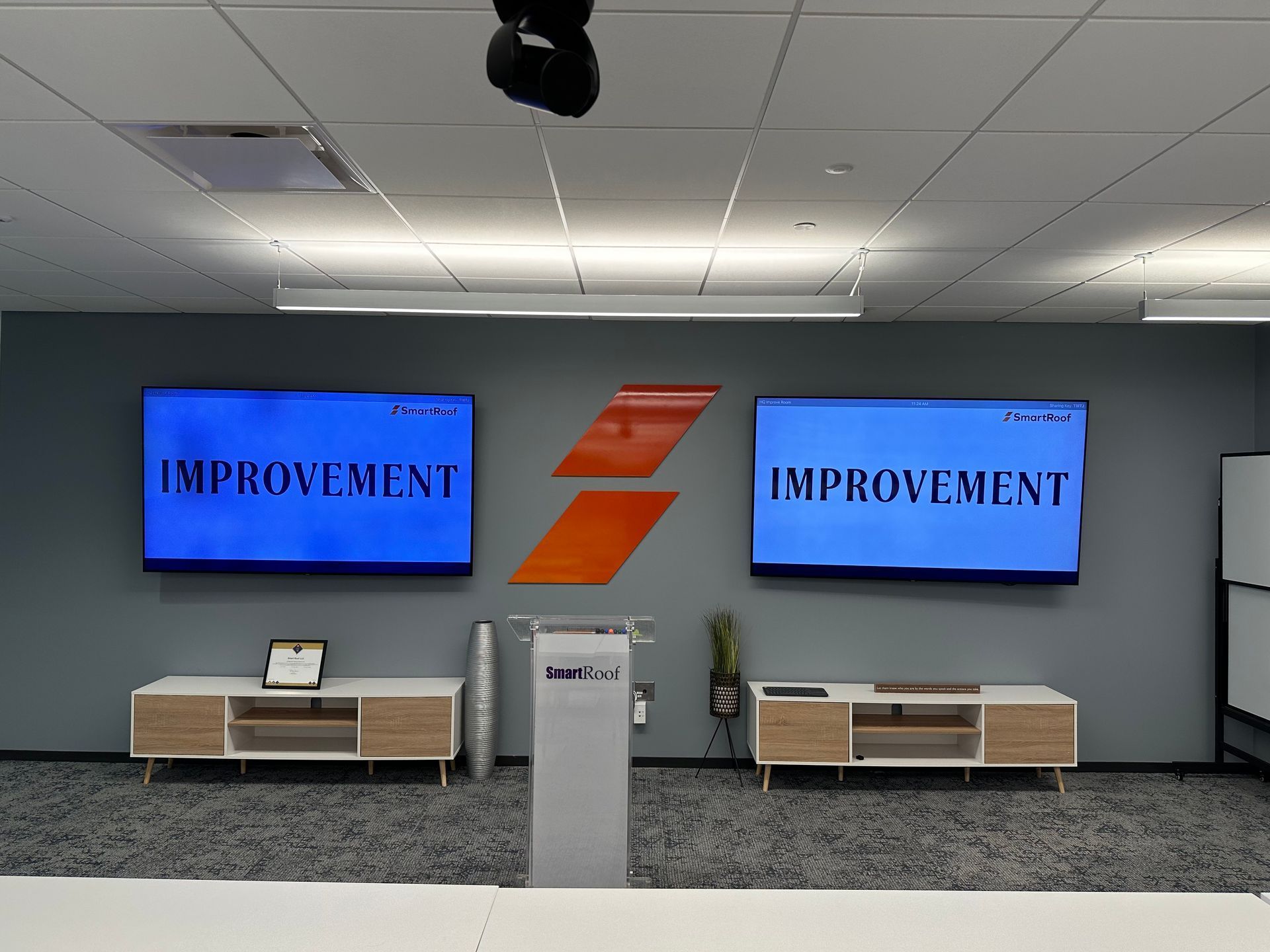 A gray wall featuring two monitors displaying the word 