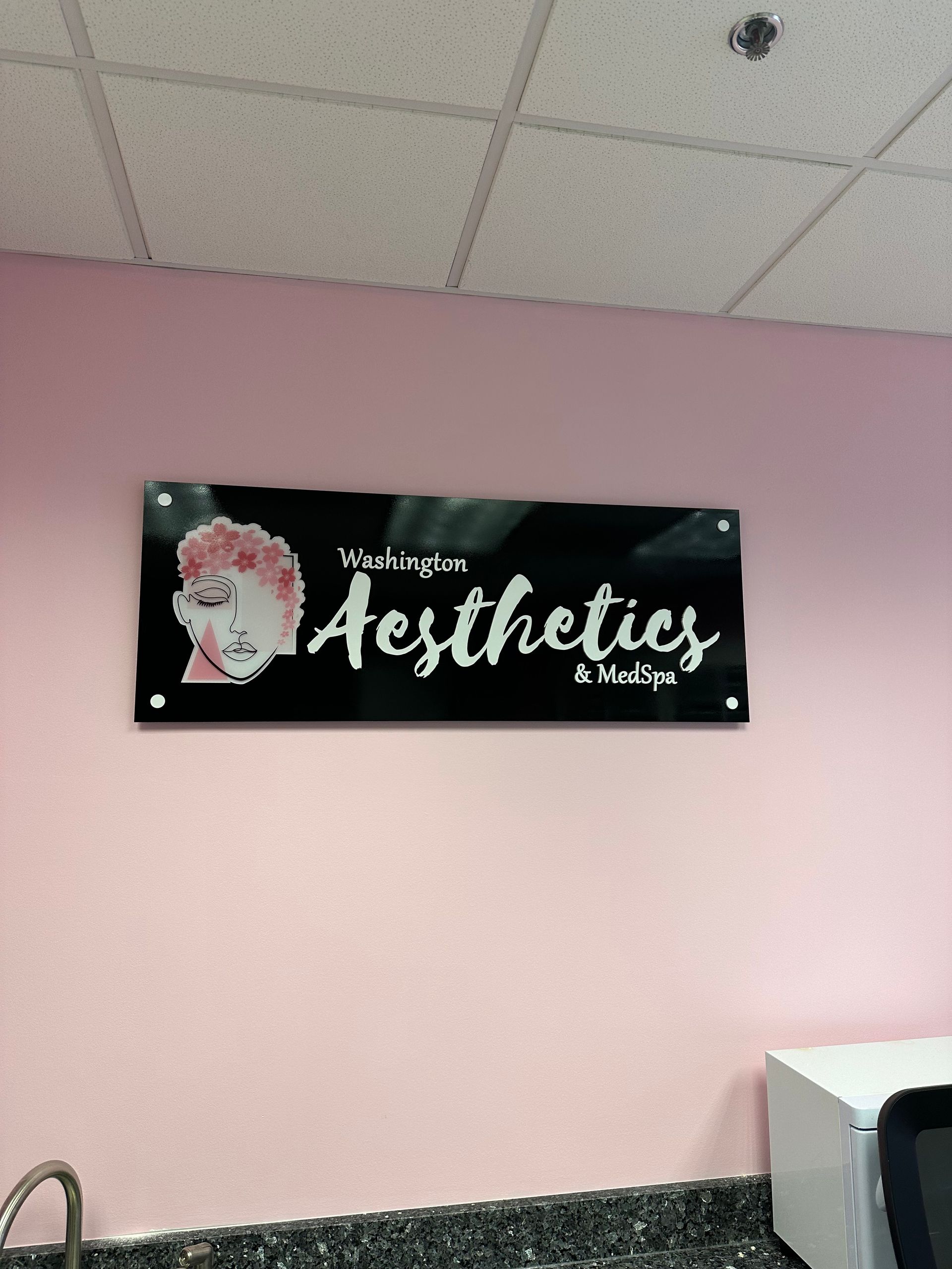 Black “Aesthetics” sign on a pink wall in a salon interior