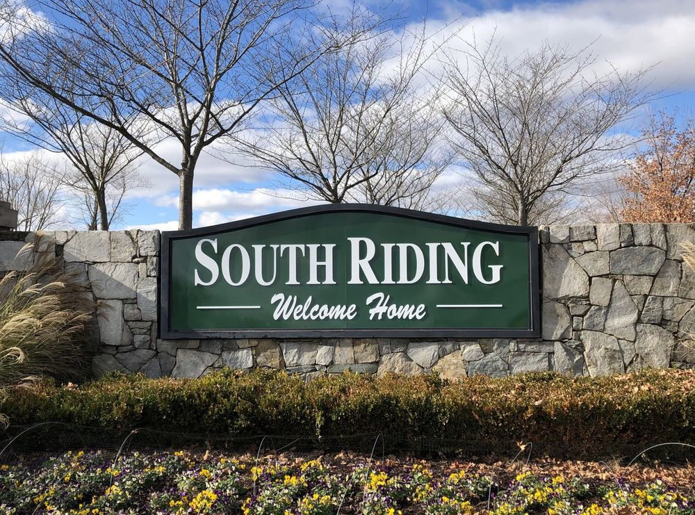 South Riding welcome sign on a stone wall with trees and flowers in front of a blue sky