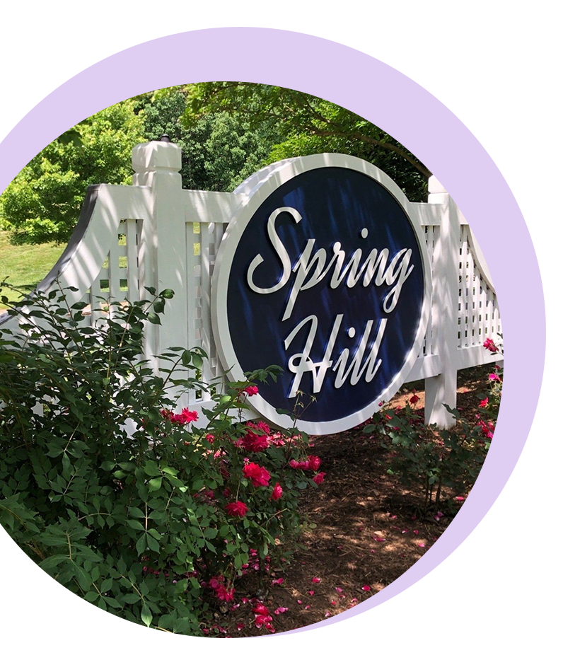 A circular image showing a white decorative fence with a round, dark blue sign that reads 