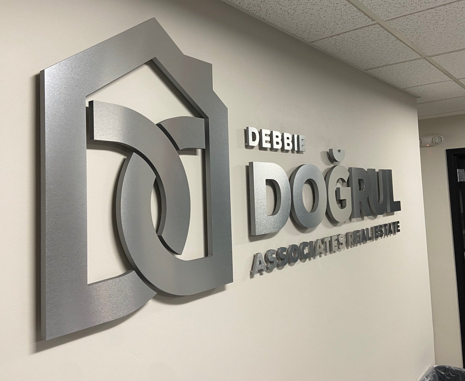 Dim wall sign reading “Debbie Dog Trials Association” in a hallway, silver 3D lettering on a gray wall
