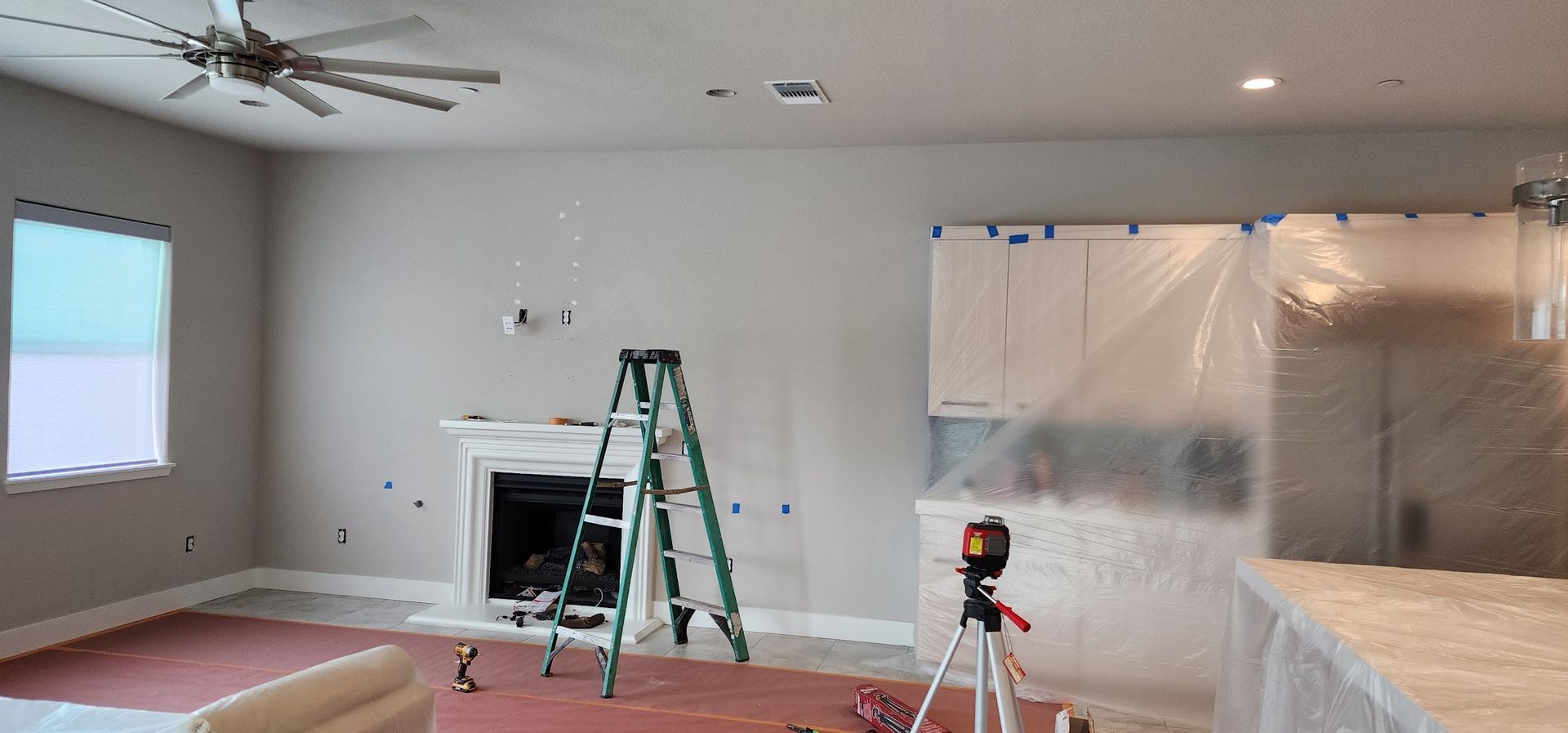A living room is being painted with a ladder and a ceiling fan.