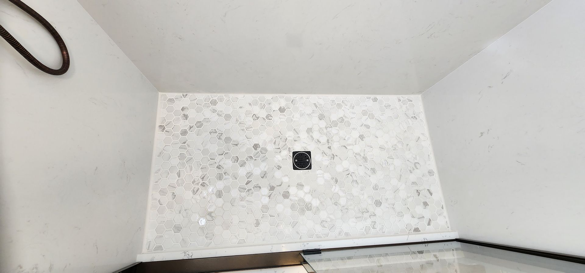 A white shower stall with a black drain in a bathroom.