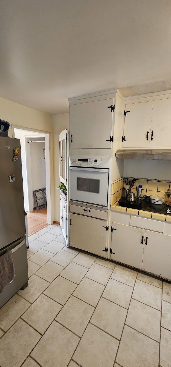 A kitchen with white cabinets , a stove , a refrigerator , and a microwave.