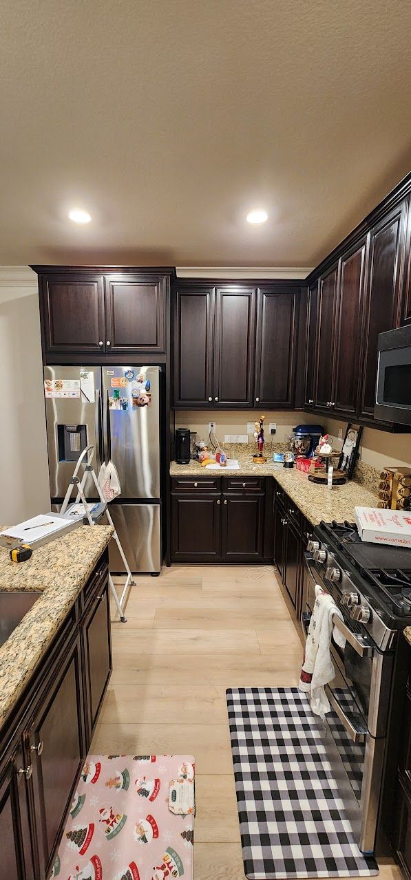 A kitchen with stainless steel appliances , wooden cabinets , granite counter tops and a checkered rug.