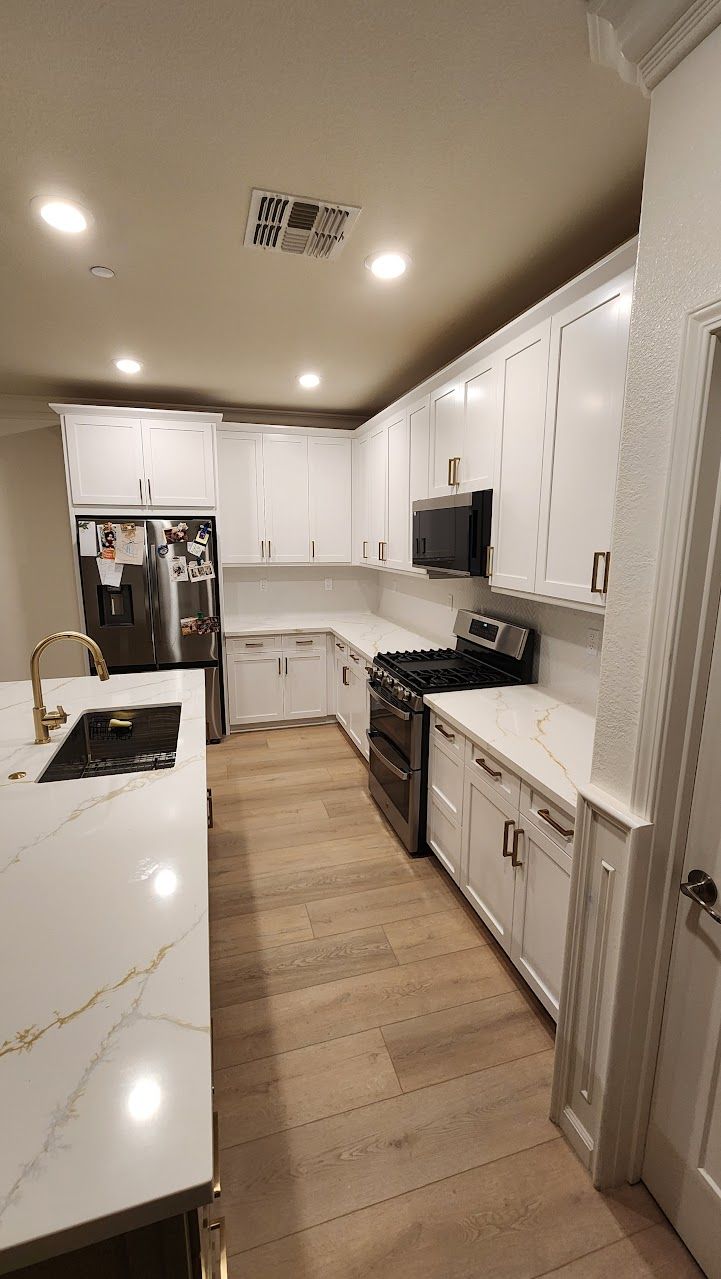A kitchen with white cabinets , a stove , a refrigerator , and a sink.