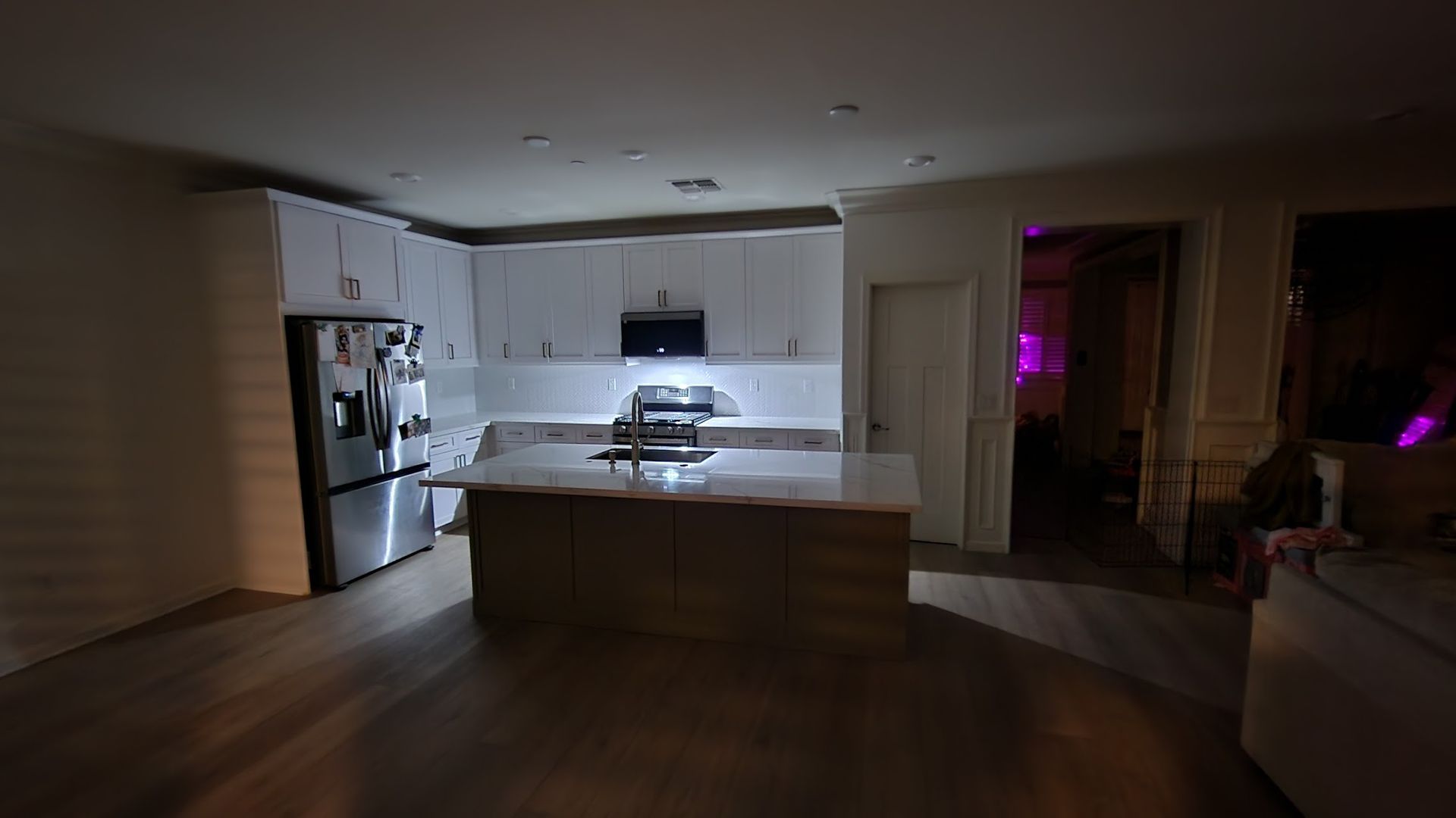 A kitchen with stainless steel appliances and white cabinets is lit up at night.