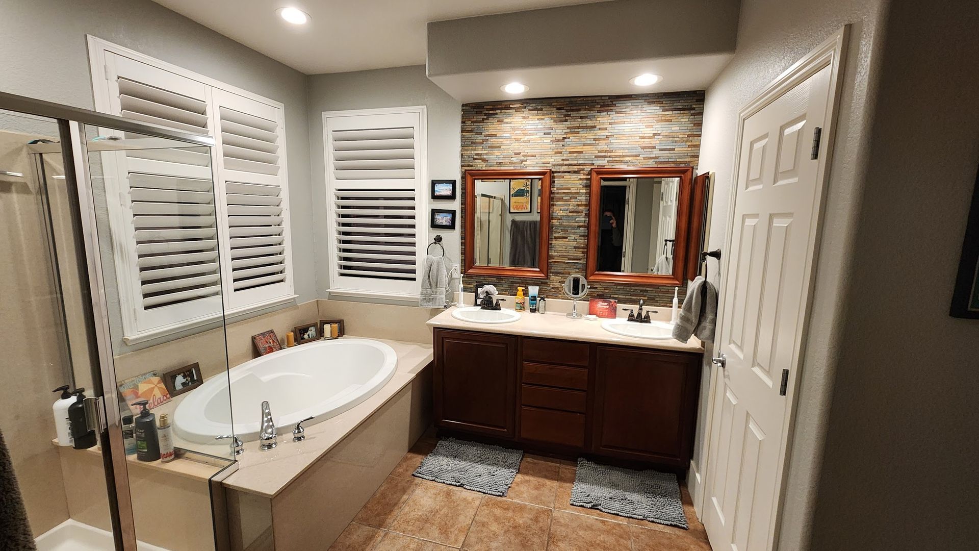 A bathroom with a tub , sinks , mirrors and shutters.