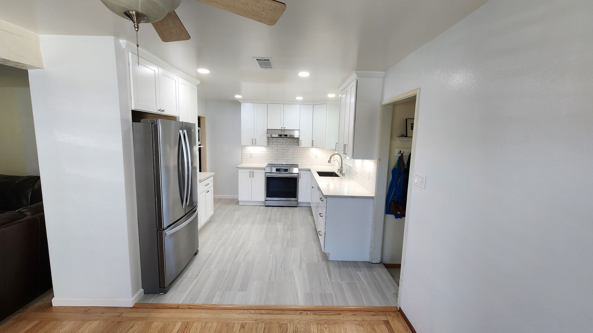 A kitchen with white cabinets , a refrigerator , a stove , and a ceiling fan.