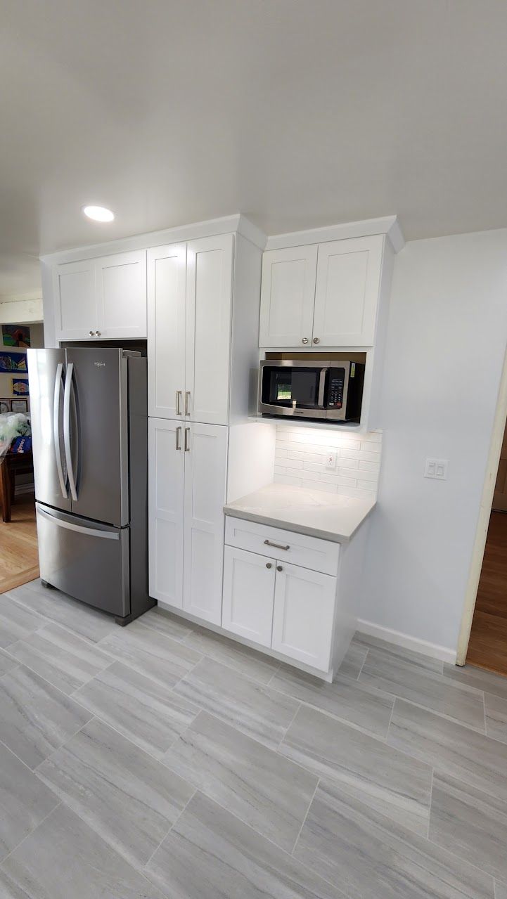 A kitchen with white cabinets , stainless steel appliances , a refrigerator and a microwave.