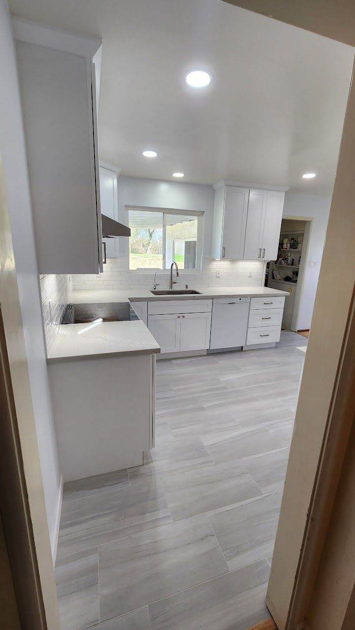 A kitchen with white cabinets , a sink , and a window.