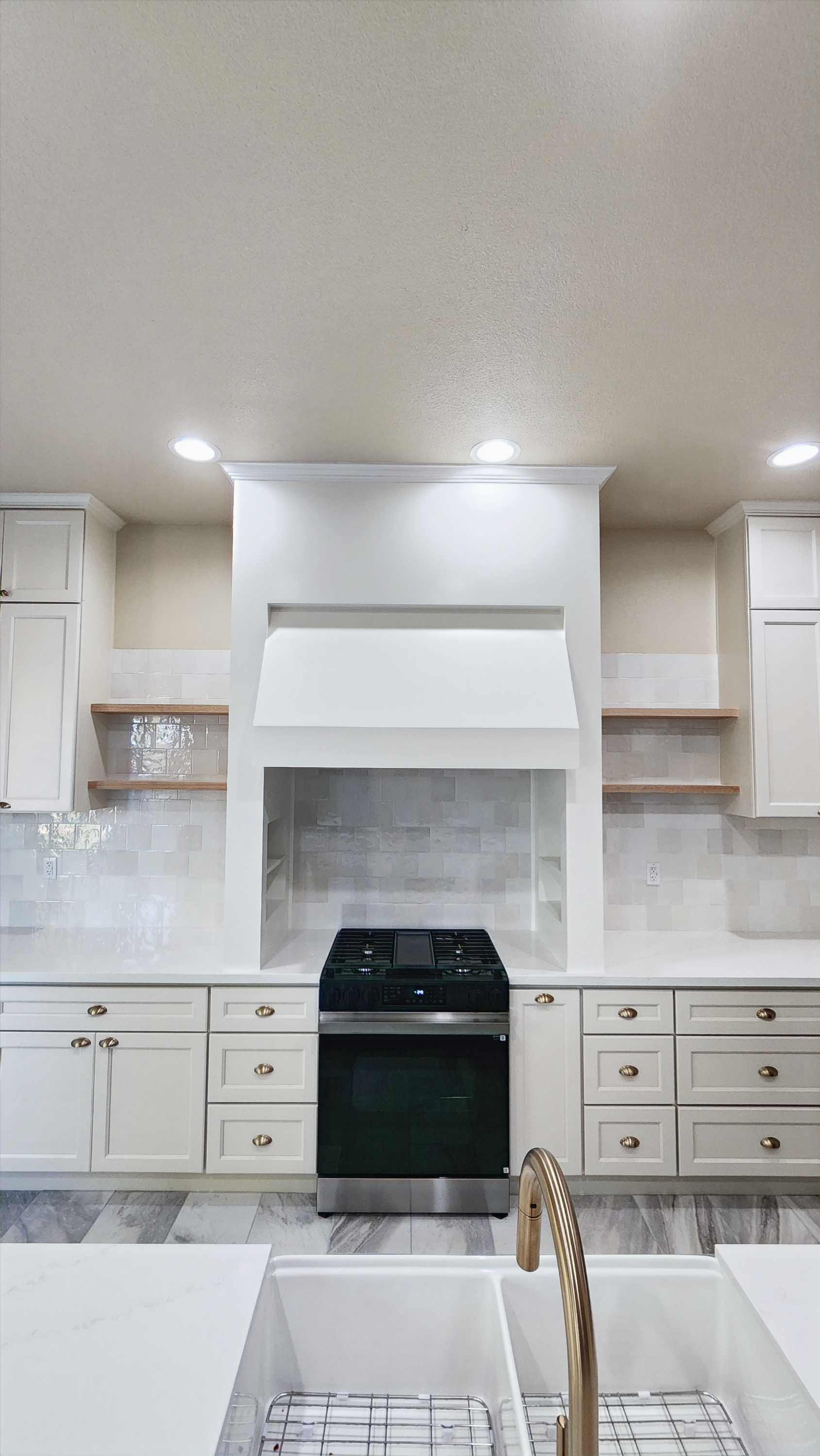 A kitchen with white cabinets , a stove , a sink and a hood.