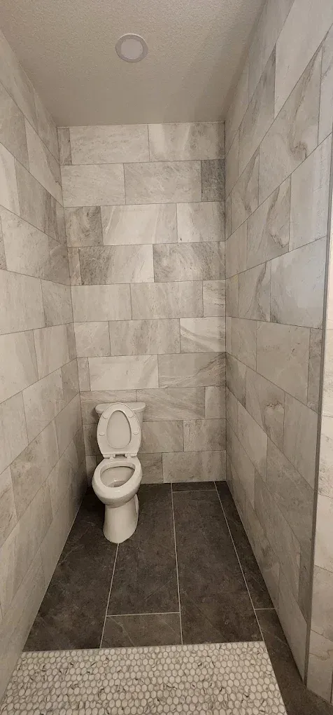 A toilet is sitting in a small bathroom with tiled walls.