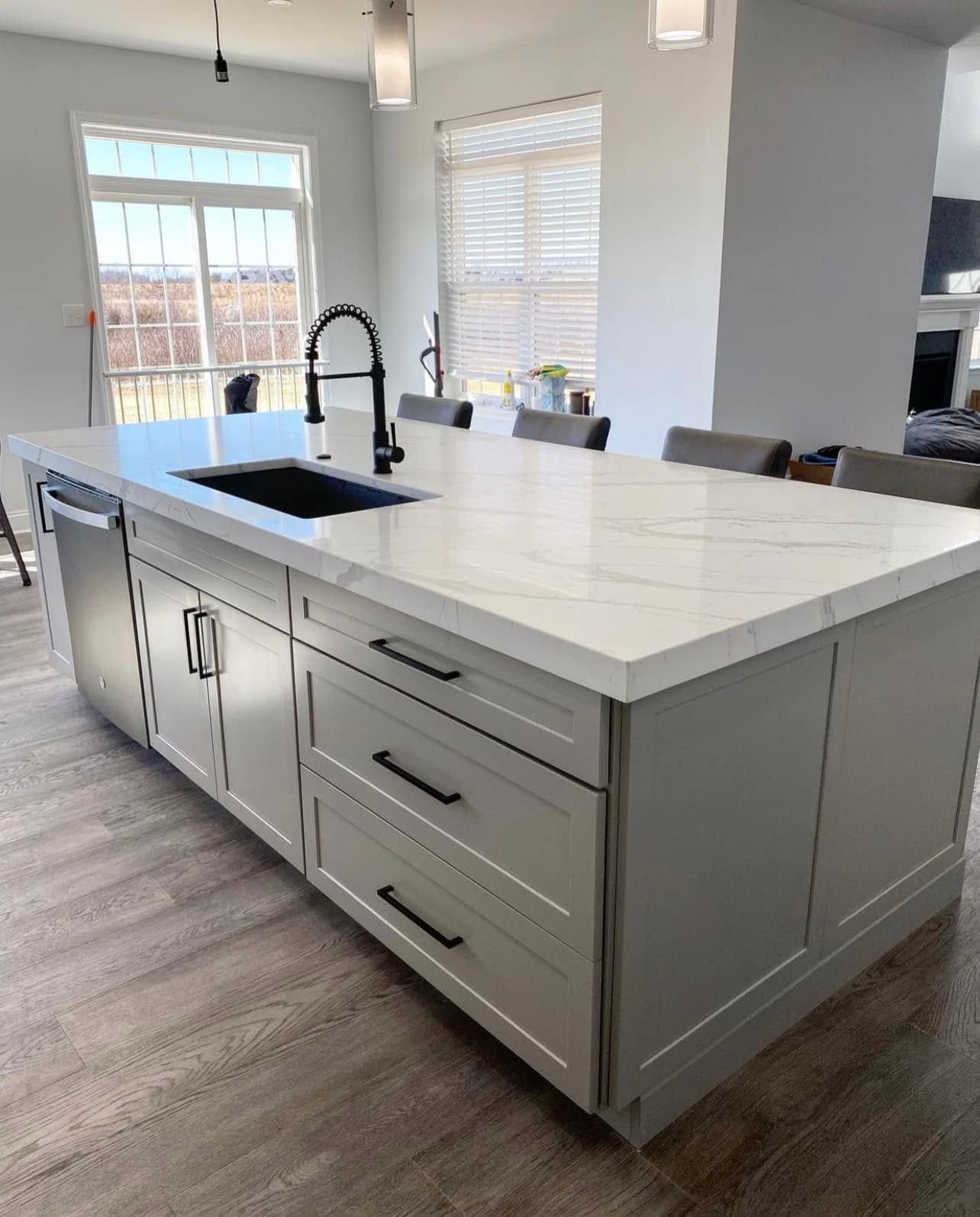 A kitchen with white cabinets , a sink , and a large island.