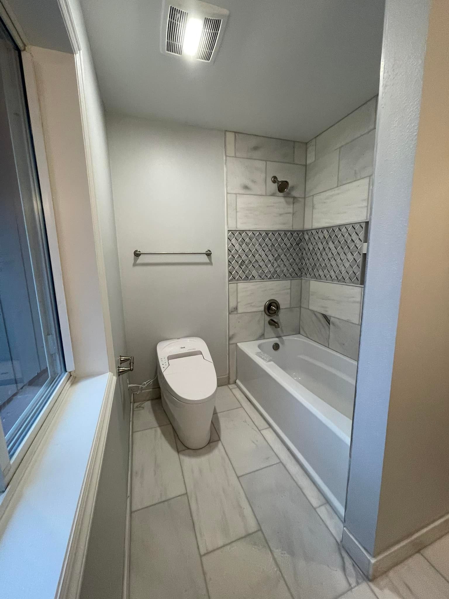 A bathroom with a toilet , tub , shower and window.