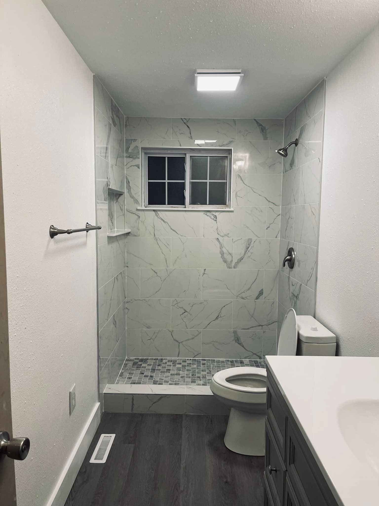 A bathroom with a toilet , sink , shower and window
