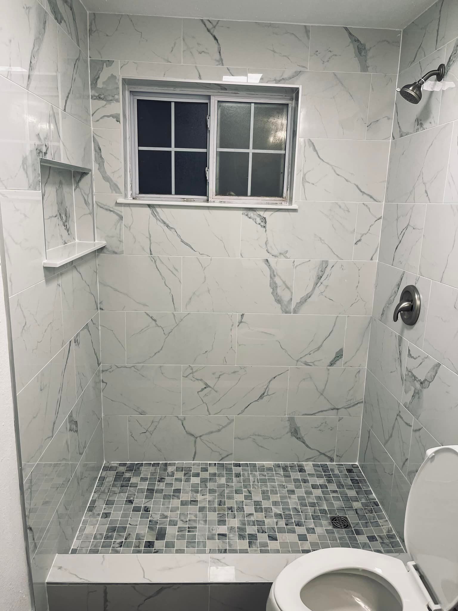 A bathroom with a toilet , shower , and window.