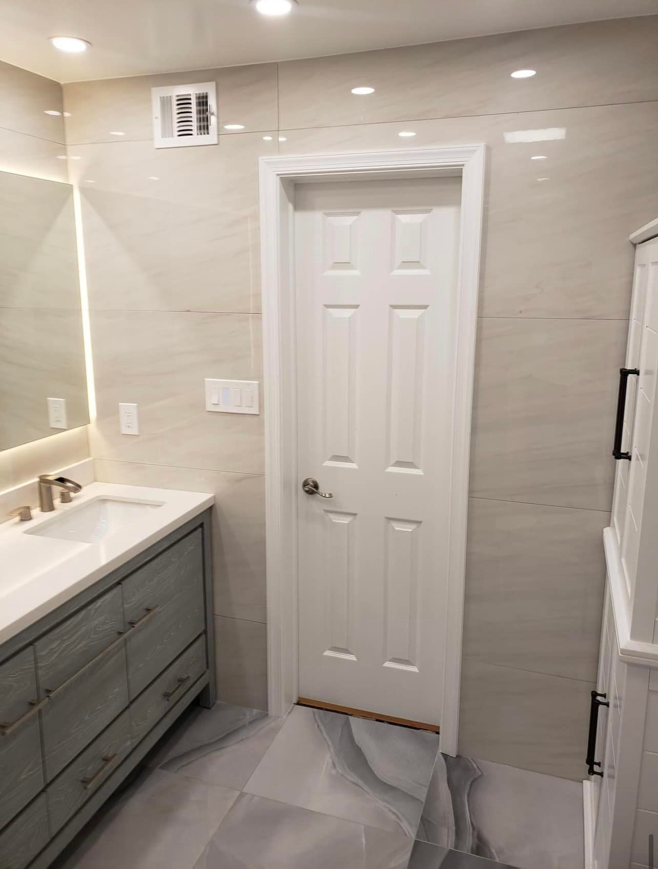A bathroom with a sink , mirror and door.