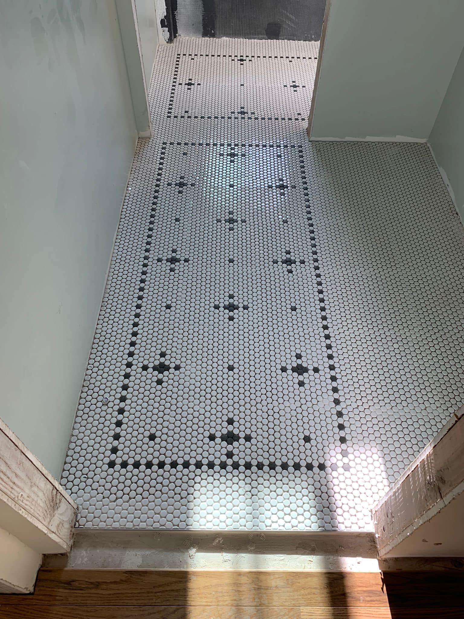 A hallway with a black and white tile floor and stairs.