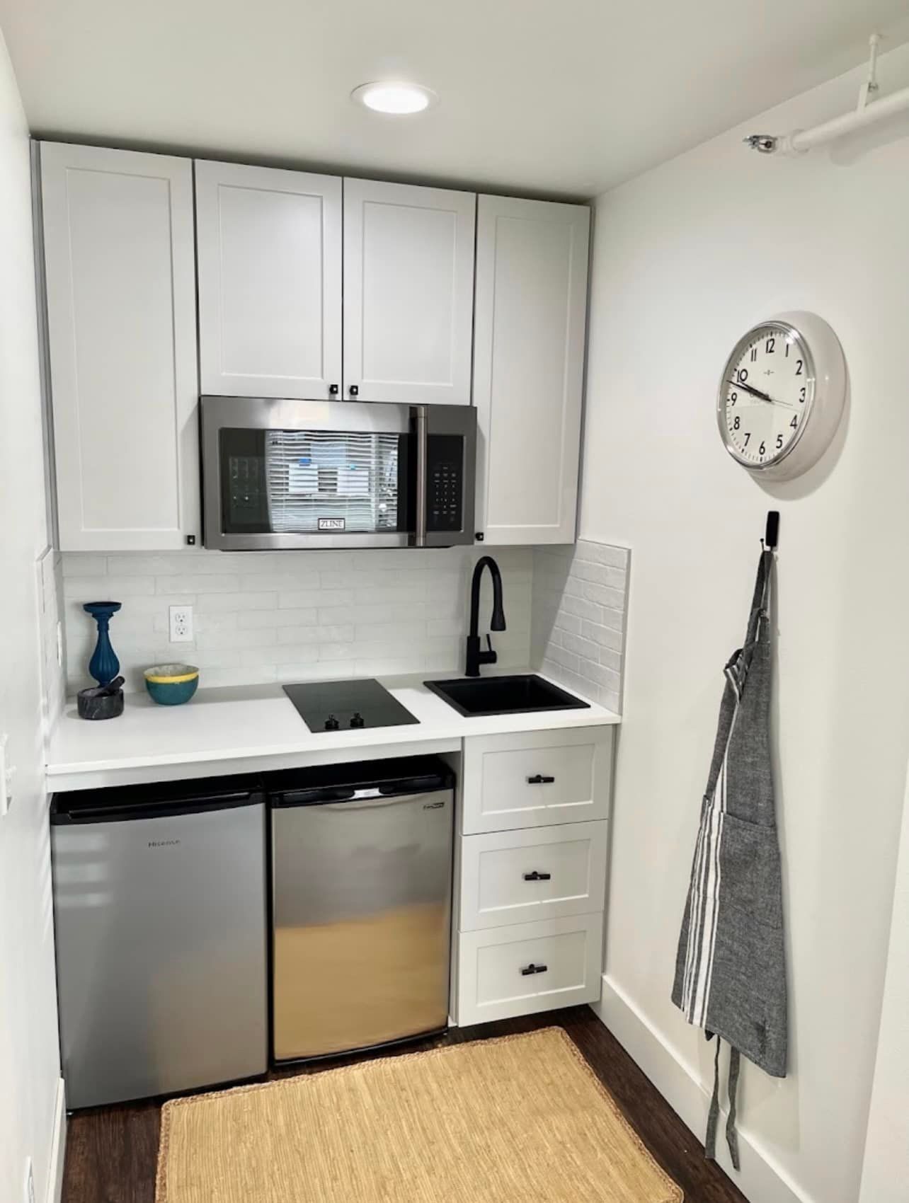 A small kitchen with white cabinets and a clock on the wall