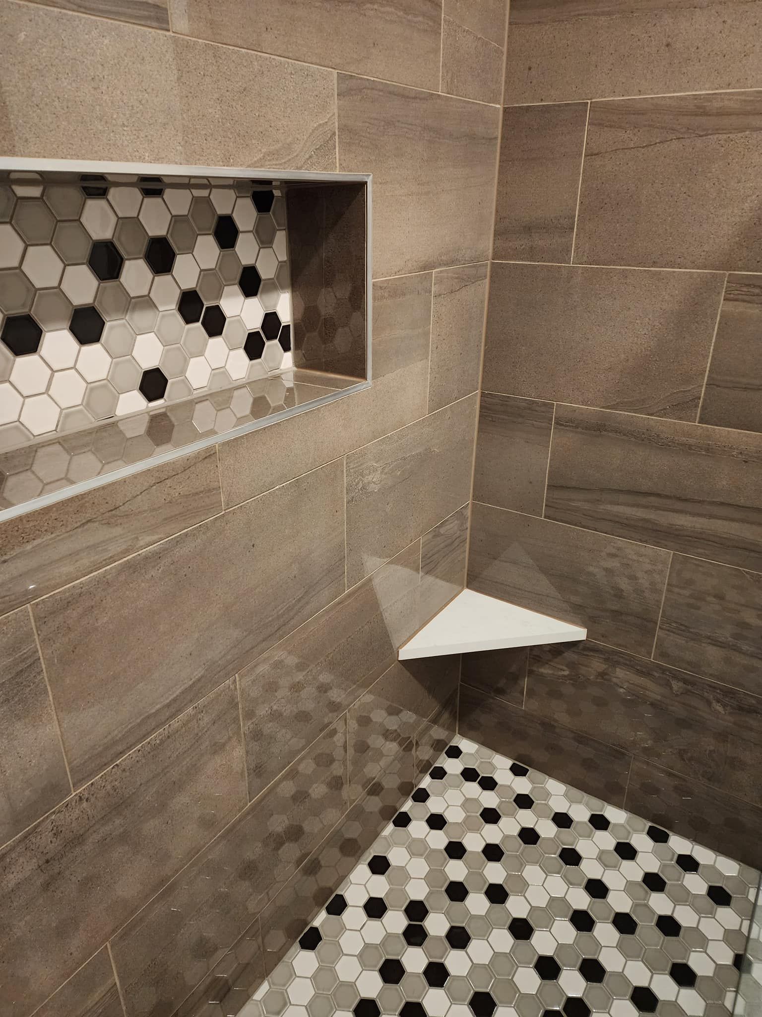 A shower with a tiled floor and a shelf in the corner.
