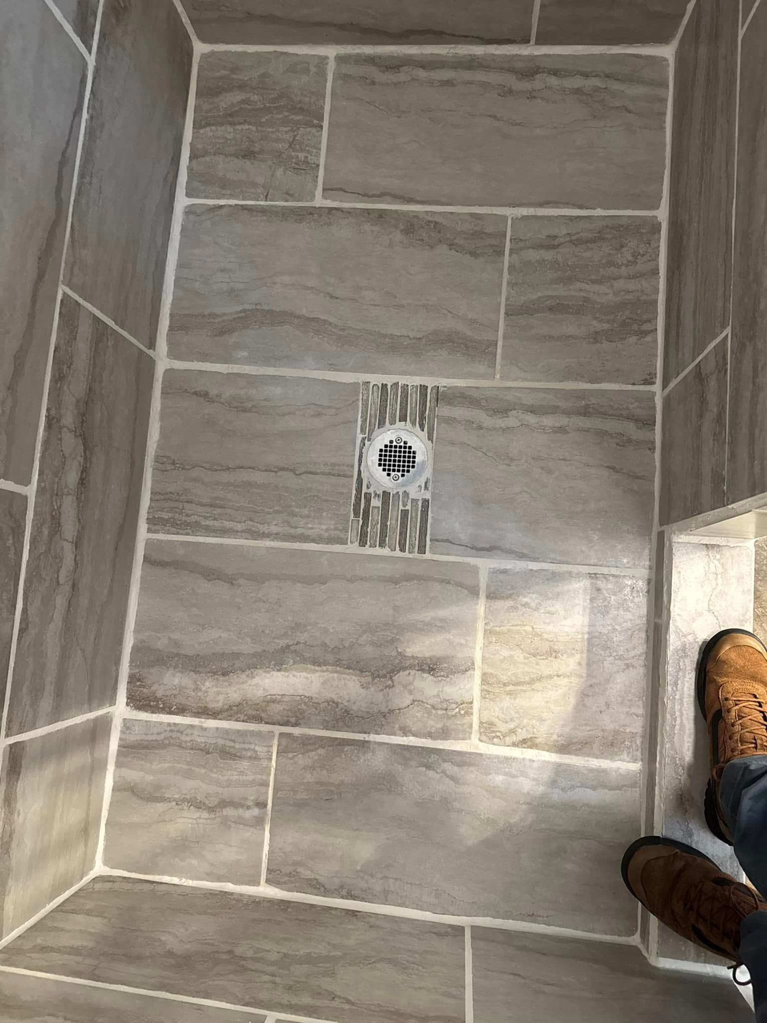 A person is standing in a tiled shower with a drain.