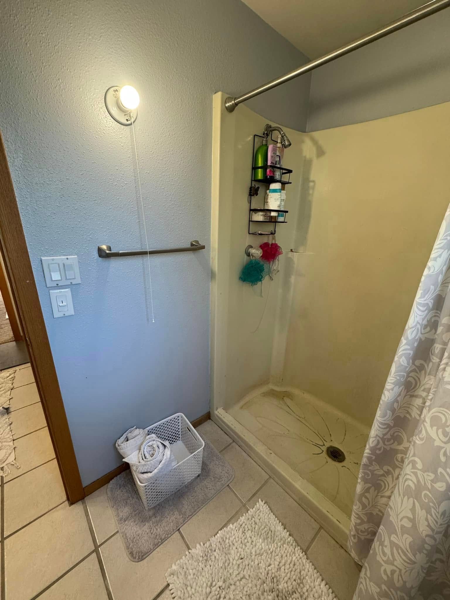 A bathroom with a walk in shower and a laundry basket.