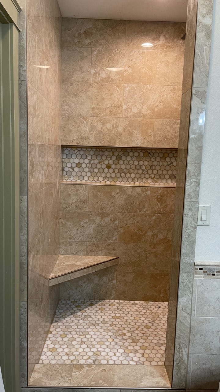 A bathroom with a walk in shower with a bench and a shelf.