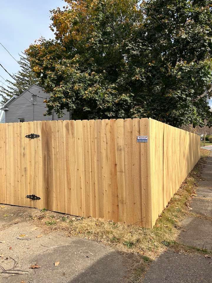 A wooden fence is sitting next to a sidewalk in front of a house.