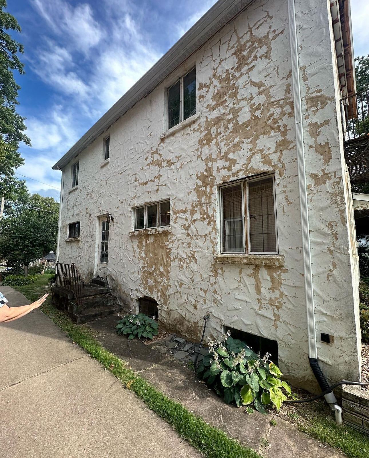 A white house with peeling paint is sitting next to a sidewalk.