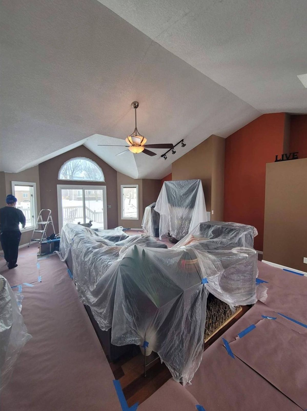 A living room is being painted and covered in plastic.