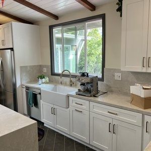 A kitchen with white cabinets , a sink , a refrigerator , and a window.