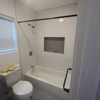 A bathroom with a toilet , tub , shower and window.