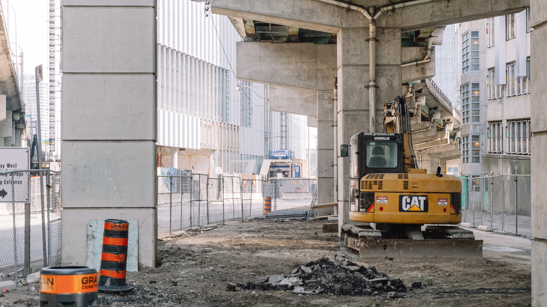 A yellow cat excavator is parked under a bridge.