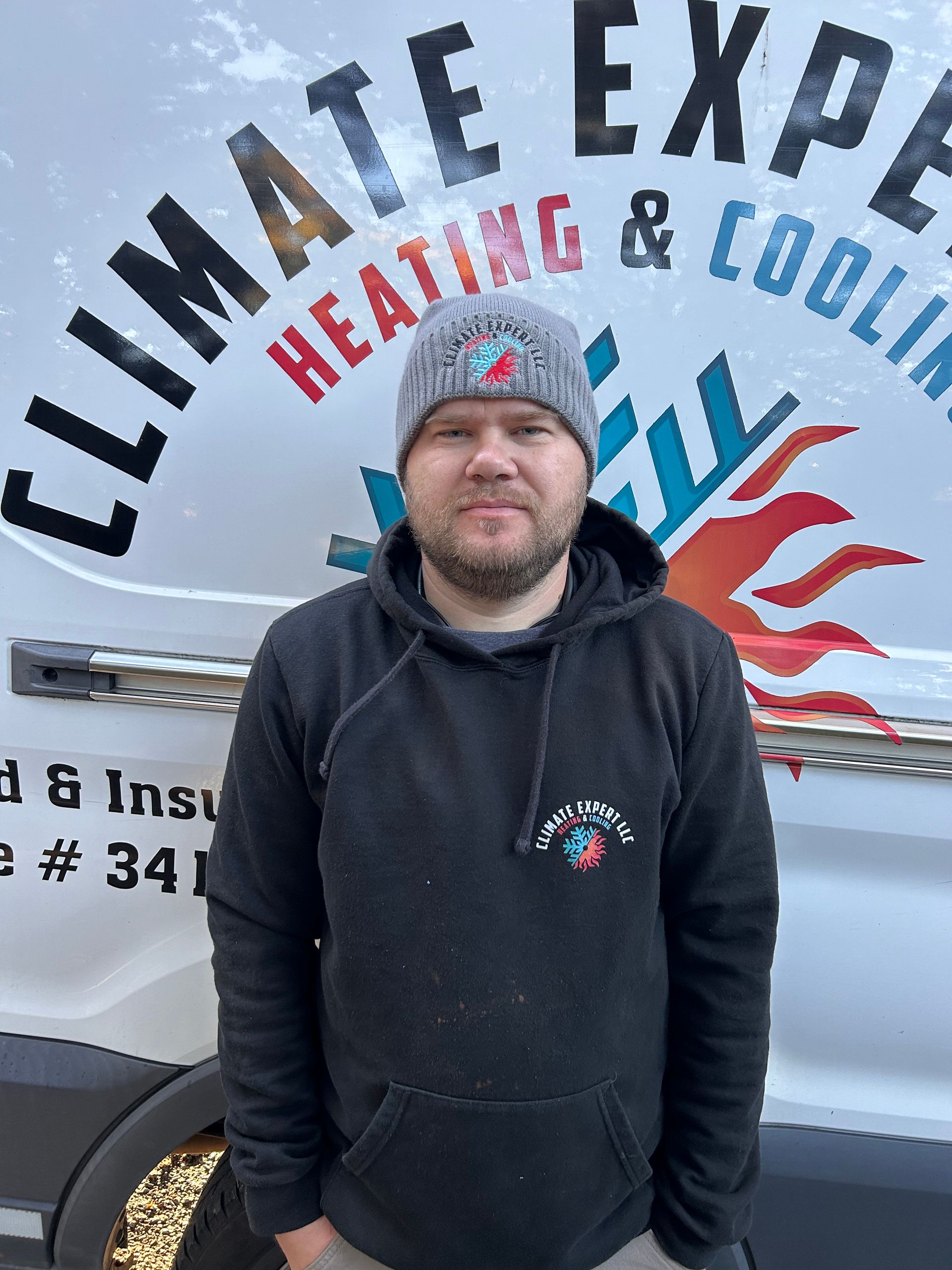 Man in beanie and hoodie stands in front of a HVAC van with 