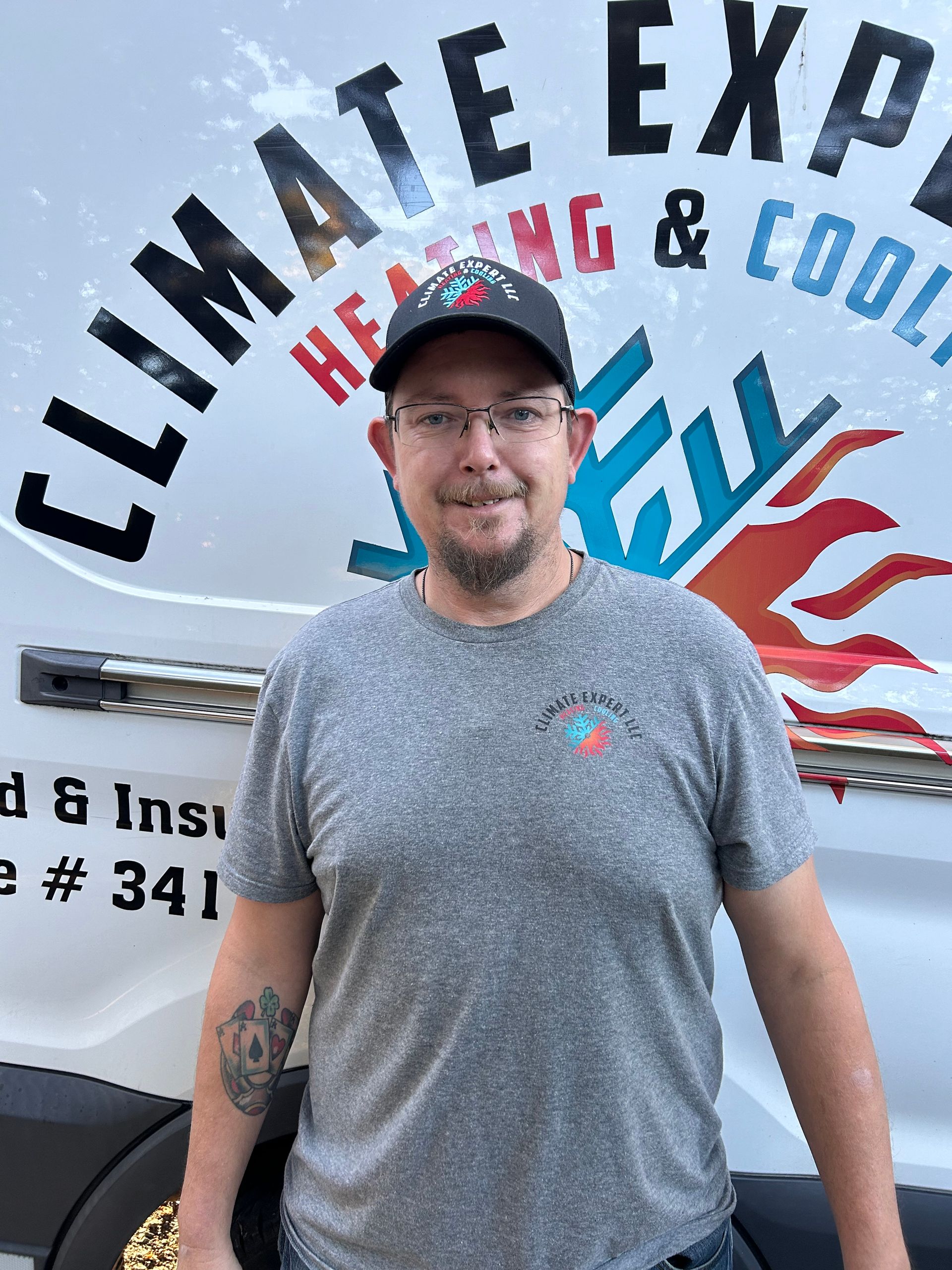 Man in gray shirt and baseball cap in front of a company van with 