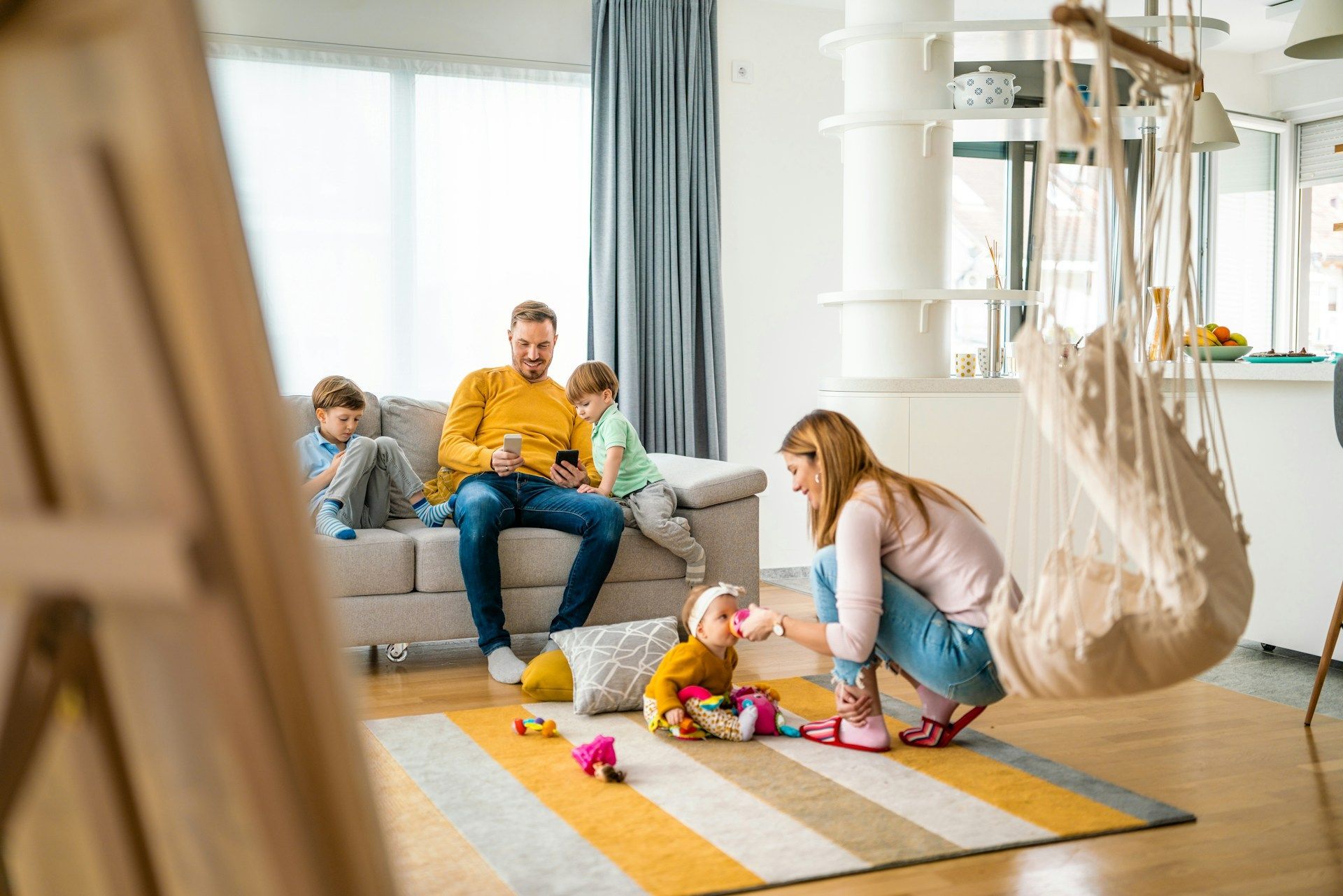 Family of three sitting on floor, interacting with a baby; near fireplace.