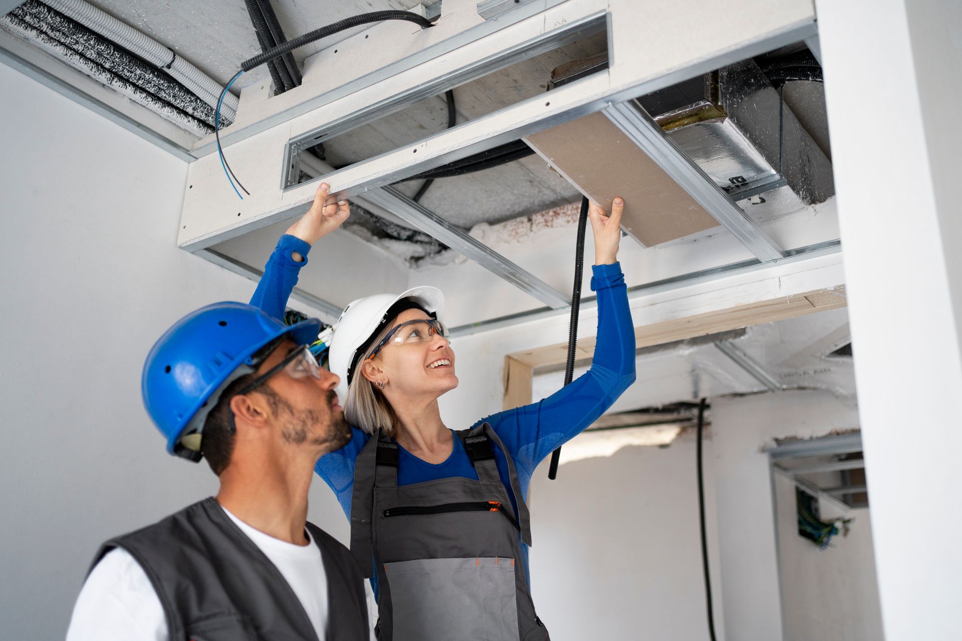 Two construction workers installing a ceiling panel in a building under construction.