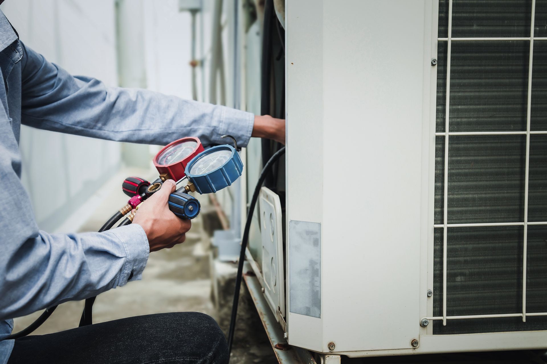 Technician checking an outdoor AC unit with pressure gauges connected to the system.