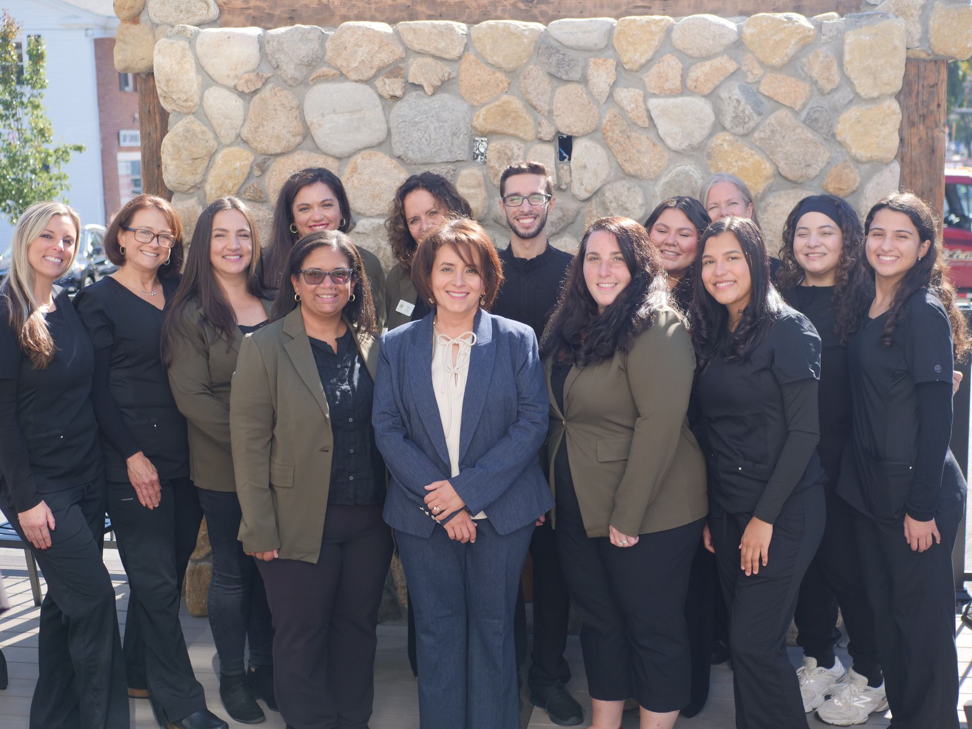 Group of people posing outdoors in front of a stone wall; some wearing suits, others casual clothing.