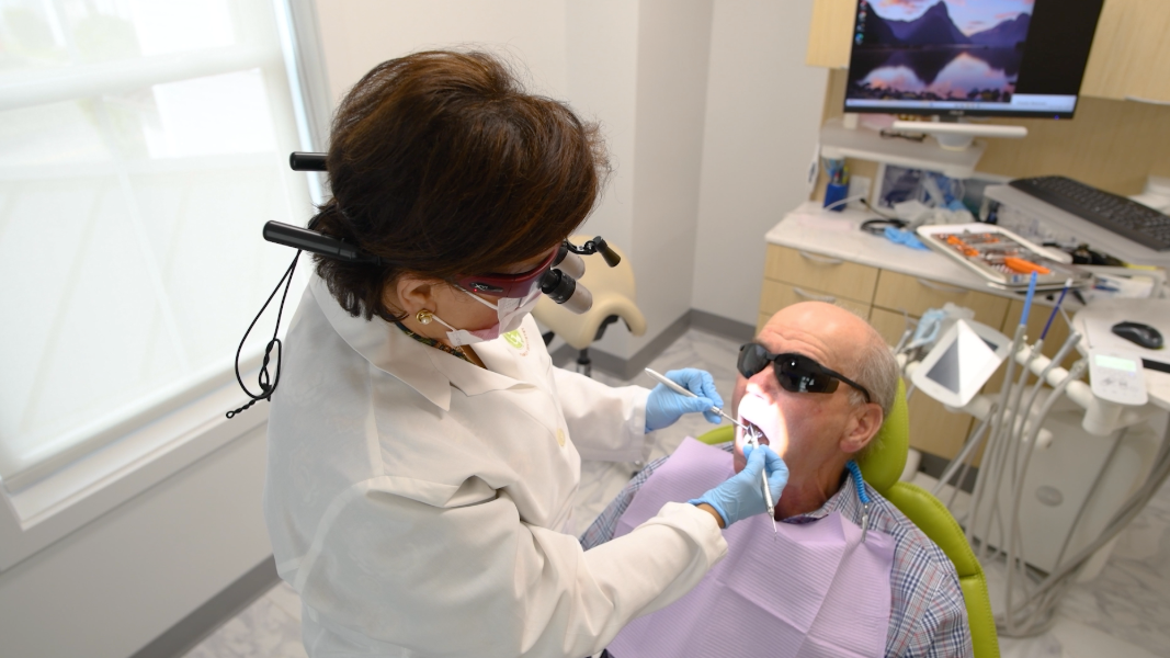 Dentist in blue scrubs examining a patient's teeth with tools; clinic setting.